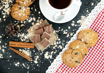 Coffee cup, homemade oatmeal cookies with raisins and cinnamon on a black table.