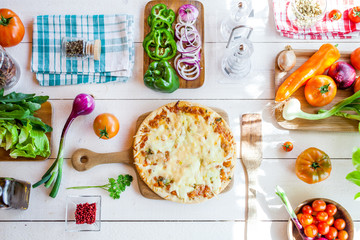 fresh homemade traditional italian cheese pizza   on wooden cooking table with ingredients. wallpaper for pizzeria and food concept. top view, flat lay