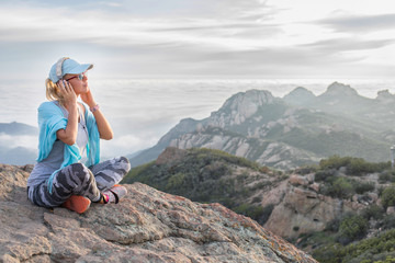 Listening to your soul: beautiful relaxed girl sitting on the mountain summit with her headset on