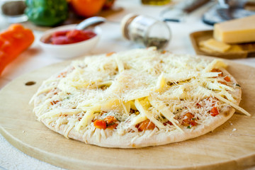closeup raw fresh homemade traditional italian cheese pizza ready to cook on wooden cooking table with ingredients. wallpaper for pizzeria and food concept