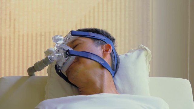 Sleep without snoring, healthcare concept.
Man laying in bed wearing CPAP mask   moving head while resting day time in living room,HD slow motion.