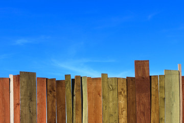Multicolored Wooden Fence And Blue Sky. A Colored Wall Of Wood With A Lot Of Copy Space. Wooden Fence And Blue Sky. Colored Painted Old Shabby Wooden Desk Background. Wooden Background.
