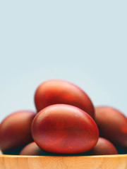 Collection of red dyed easter eggs hand painted in a wooden bowl on light blue sky  background, macro, close-up. Onion husk of the paint. Set, pile of eggs