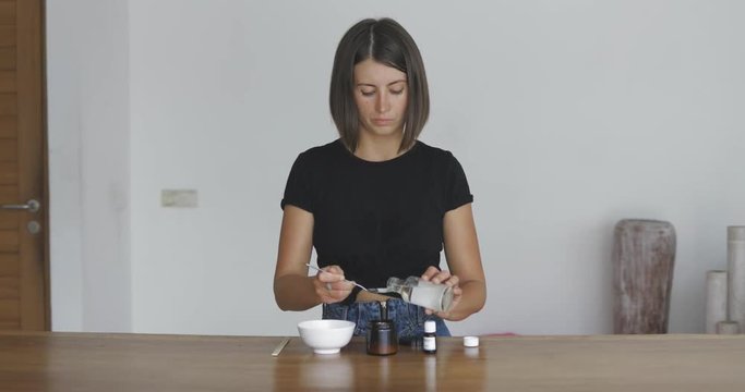 Young pretty woman makes toothbrush independently from ecological natural materials at home. Girl pours coconut oil into jar. Zero waste concept