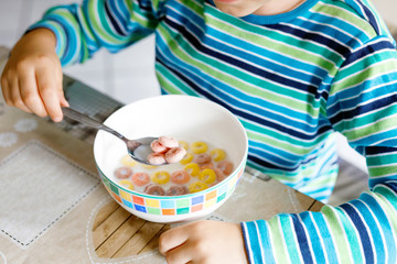 little blond school kid boy eating cereals with milk and berries, fresh strawberry for breakfast