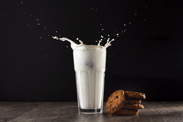 Oatmeal cookies lie on a wooden table on a black background. Near the glass of milk. Spray the milk from the glass. - Powered by Adobe