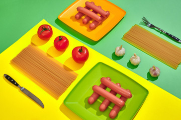 A lot of raw sausages on plate. On green and yellow background with pasta and vegetables, top view.