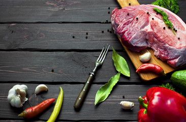 Raw meat with herbs, fresh vegetables, avocado, pepper, coriander, dill, garlic, chili and spices on a dark wooden background. Raw steak from pork or beef. Cooking concept. Top view. Copy space