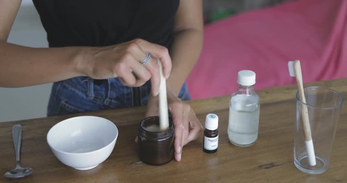 Young pretty woman makes toothbrush independently from ecological natural materials at home. Close-up of footage of girl stirring ingredients in jar. Zero waste concept