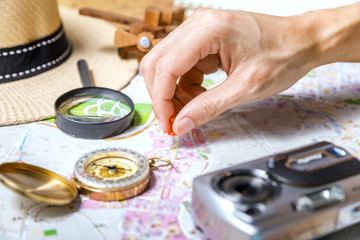 Fototapeta na wymiar Hand attached pushpin on location of a destination point on a map - Travel plan, trip vacation, tourism mockup - Outfit of traveler