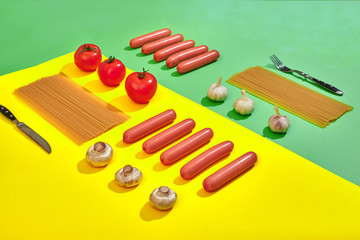 A lot of raw sausages with pasta and vegetables on green and yellow background, top view.