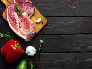 Raw meat with herbs, fresh vegetables, avocado, pepper, coriander, dill, garlic, chili and spices on a dark wooden background. Raw steak from pork or beef. Cooking concept. Top view. Copy space