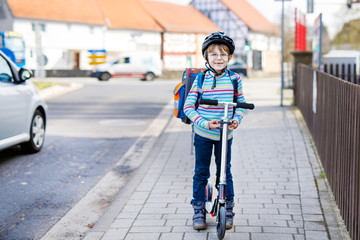 Little kid boy in helmet riding with his scooter in the city