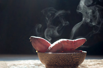 The steam from Purple Colored Sweet Potatoes on bowl wood dark background,noise,grain