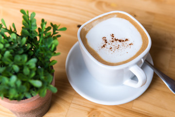 Hot cappuccino cup with tree vase on wooden table top view