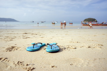 The blue slippers on the beach with white sand, against the background of the sea.
