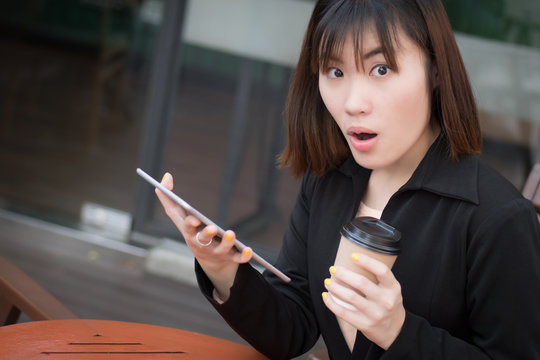 happy laughing business woman using computer tablet; portrait of excited surprised happy laughing business woman in suit working with her mobile computer tablet; asian Chinese young adult woman model