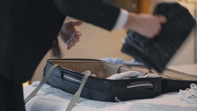 Crop view of man in elegant suit packing bag on bed preparing for traveling.