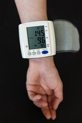 Woman hand with electric tonometer measuring blood pressure. Medicine, age, healthcare and people concept with tonometer and pills suggesting to take care of blood pressure.