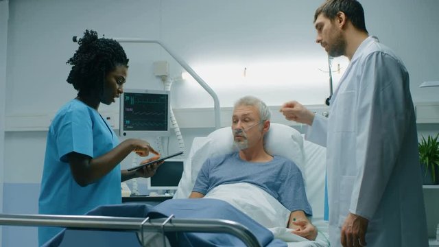 In the Hospital, Senior Man Lying in the Bed, Talks with Doctor and Nurse who Use Tablet Computer. Technology Helps Cure Patients, Modern Hospital Ward. Shot on RED EPIC-W 8K Helium Cinema Camera.