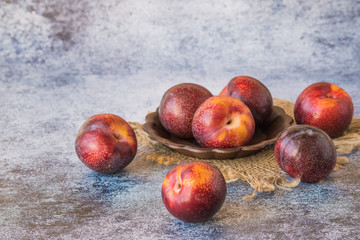 Fresh large ripe plums in a small round vase on a napkin from a burlap on a blue background.