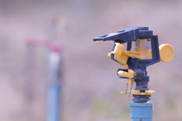 sprinkler closeup and water spray, with blurry background in field.