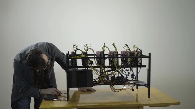 Young man in work coat maintains a mining rig with six powerful graphics cards, with a lot of love and attention he uses pump and brush and gently clean off the dust that you do not see, symbolic shot