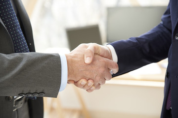 Handshake. Close-up shot of two businessman wearing suit and shaking hands at office.