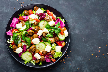 Fresh vegetable salad with mushrooms and mozzarella on black plate. Fried champignons with vegetable salad