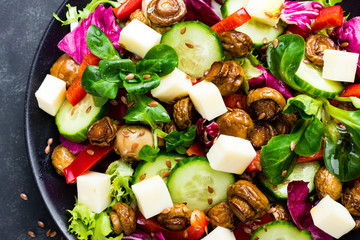 Fresh vegetable salad with mushrooms and mozzarella on black plate. Fried champignons with vegetable salad