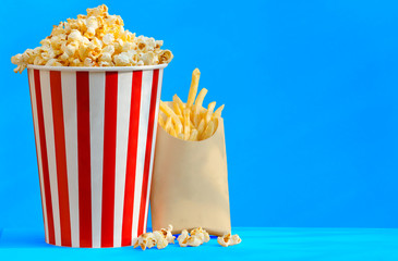 popcorn in striped bucket and french fries on blue table background with soft sunlight