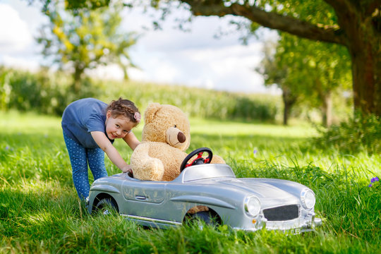 Little preschool kid girl driving big toy car and having fun with playing with big plush toy bea