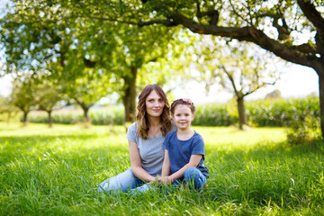 Fototapeta premium Beautiful young mother and little daughter sitting on green grass and resting