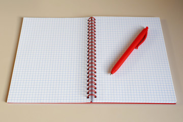 Top view closeup of open notebook with blank pages, spiral, red cover and red pen on light brown beige desk background with space for text. Business or education concept.