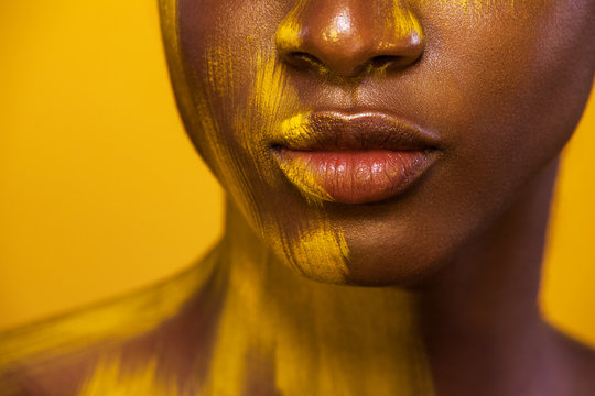 Closeup lips portrait. Cheerful young african woman with yellow makeup. Female model against yellow background.