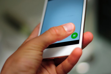 Close-up of phone hold in one hand with button to create a new chat message. Blurry background