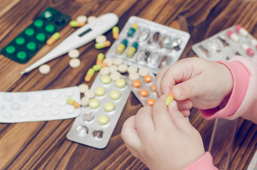 Children's hands with medicines on a wooden table. A small child left unattended plays dangerous drugs
