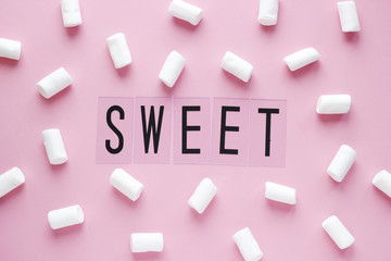 White marshmallows and SWEET word on pink pastel background. Food concept in minimal flatlay style. Horizontal image top view.