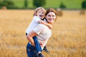 Mother holding kid boy on arms on wheat field in summer