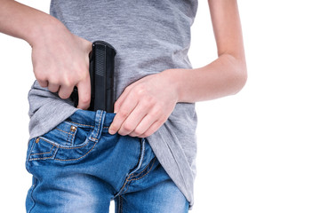 Juvenile hands shoved a real gun in the waistband of jeans, close-up, isolated on a white background