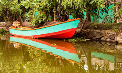 Small boat sits in water under trees with reflections in water