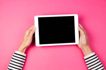 Woman's hands with tablet computer on pink background.