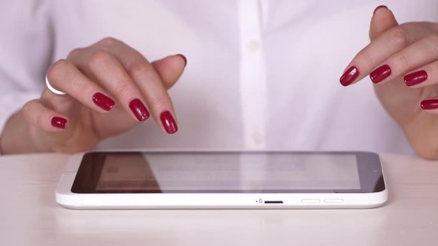 The woman in a white shirt watches information on the tablet. The businesswoman works at office or at home. Typing on the tablet. Hands close up. hand touching tablet computer surface touchscreen. The