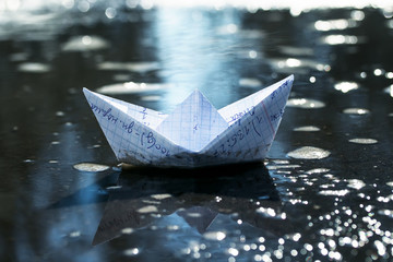 children's school the little paper boat of cellular notebooks swims in blue water of early spring puddle