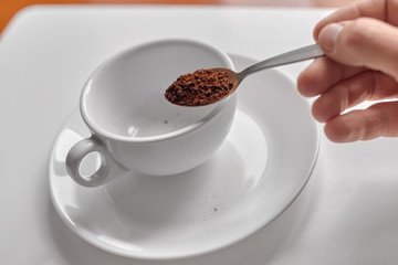 Hand pouring instant coffee from spoon in cup