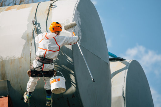 Industrial climber in helmet and uniform painting water tower. Professional Painter working on height. Risky job. Extreme occupation.