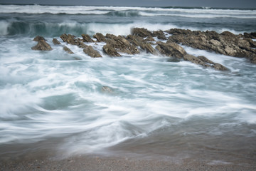 scenic atlantic coastline with waves in motion around rocks on sandy beach in long exposure, bidart, basque country, france