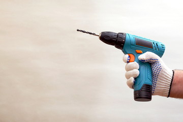 hand in dotted work glove holding cordless drill machine on gray background, copy space