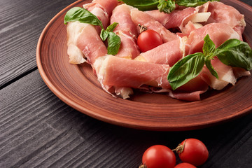 Small pieces of pineapple rolled in jamon iberico or proscuitto with cherry tomatoes and spanac leaves on a plate