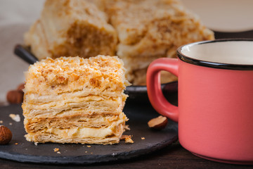 Slices of sweet classic layered cake Napoleon, metal mug and hazelnuts 